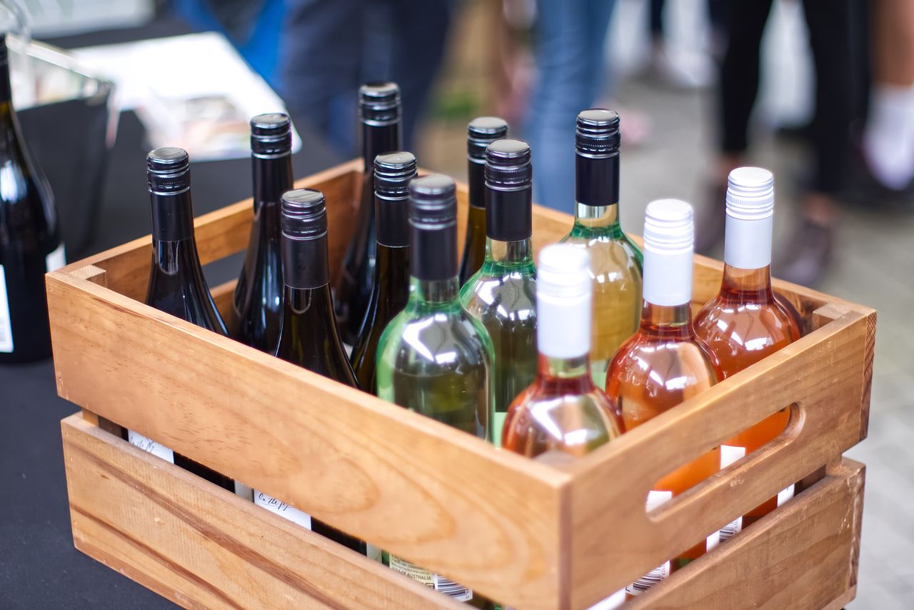Home A wooden crate filled with diverse wine bottles at an outdoor gathering.